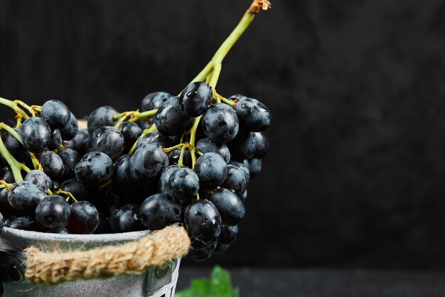 Un secchio di uva nera con foglie su sfondo scuro. Foto di alta qualità