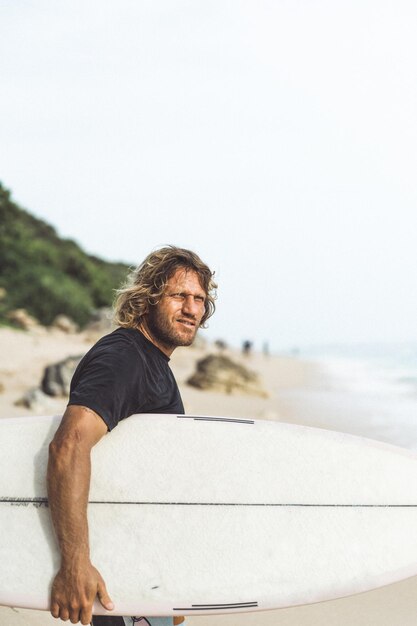 Un surfista uomo con i capelli ricci bianchi con una tavola da surf sta per fare surf.