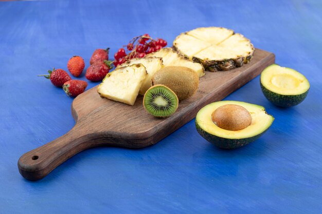 Un tagliere di legno affettato ananas con kiwi sulla superficie blu