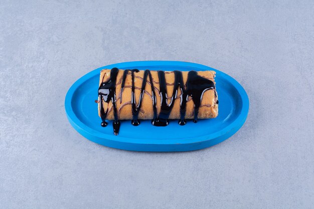Un tagliere di legno blu di dolce delizioso rotolo con sciroppo di cioccolato e panna.