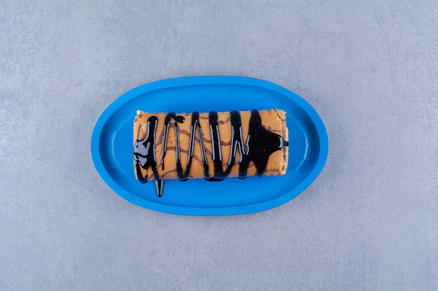 Un tagliere di legno blu di rotolo delizioso dolce con crema e sciroppo di cioccolato.
