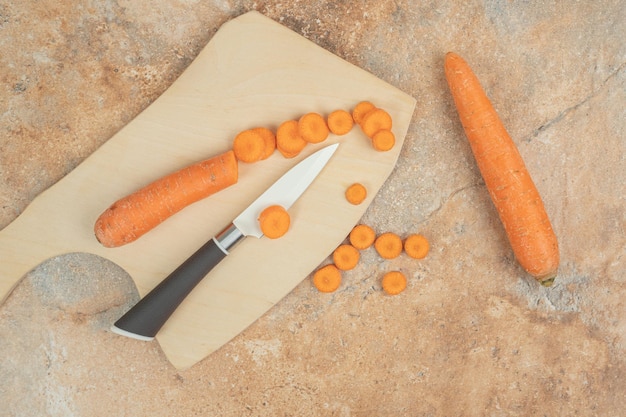 Un tagliere di legno con carota a fette e coltello