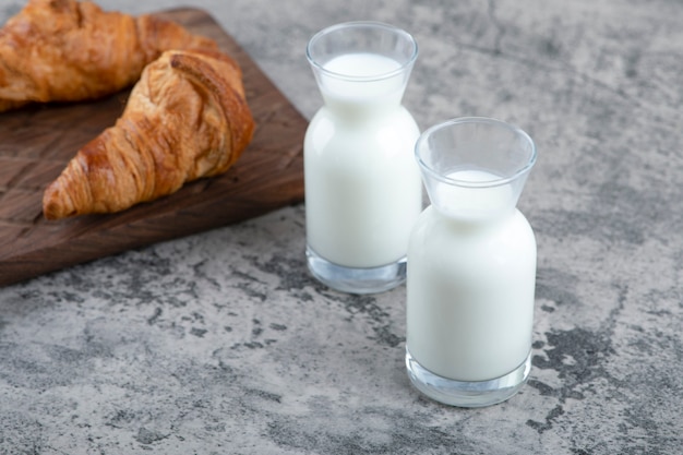 Un tagliere di legno di croissant freschi e brocche di latte in vetro bianco.