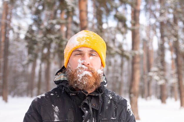 Un uomo adulto con la barba in una foresta invernale affronta tutti nella neve, congelati, insoddisfatti del freddo