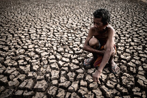 Un uomo anziano seduto abbracciando le ginocchia si chinò sulla terra sterile, il riscaldamento globale