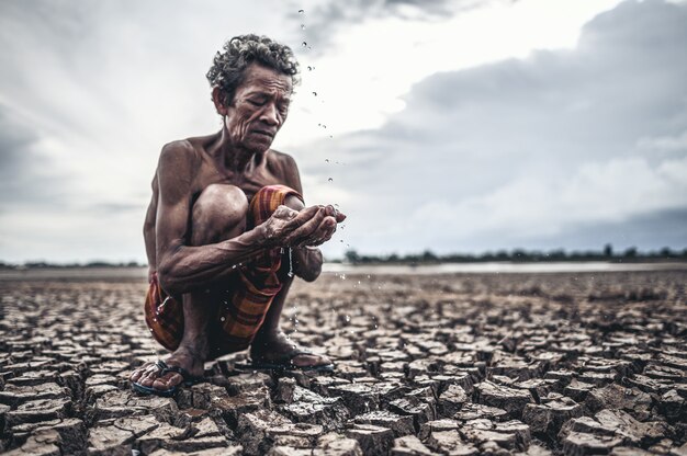 Un uomo anziano seduto in contatto con la pioggia nella stagione secca, riscaldamento globale, messa a fuoco selettiva