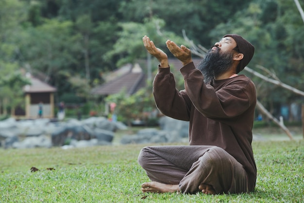 Un uomo barbuto sta meditando sull'erba verde