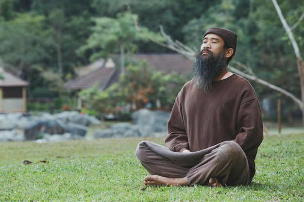 Un uomo barbuto sta meditando sull'erba verde