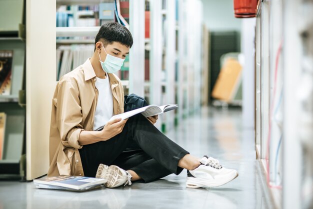 Un uomo che indossa le maschere è seduto a leggere un libro in biblioteca.