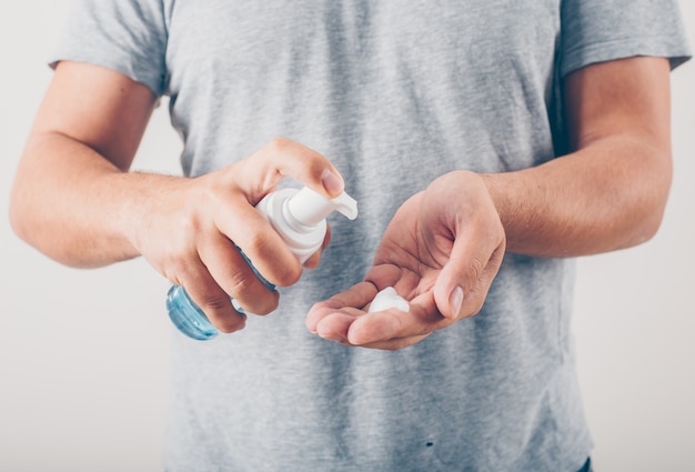 Un uomo che versa sapone liquido alla sua mano nel fondo bianco in maglietta grigia.