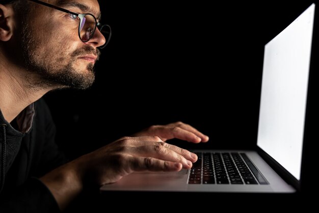 Un uomo con gli occhiali lavora al computer al buio