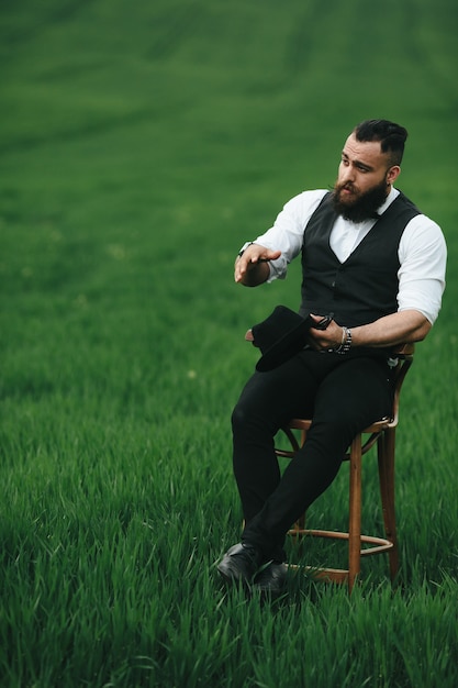 Un uomo con la barba, che pensa in un campo vicino a una sedia