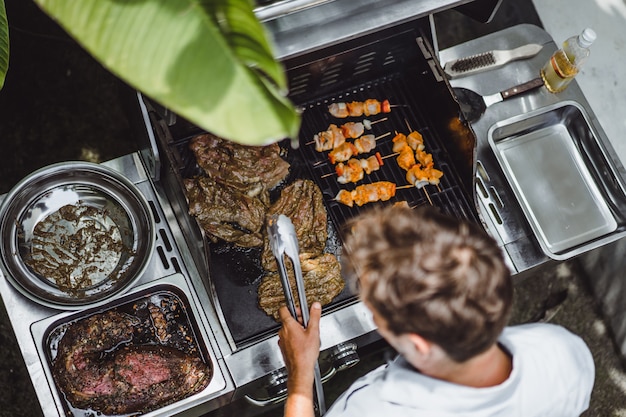 Un uomo con tatuaggi fa carne alla griglia all&#39;aperto.