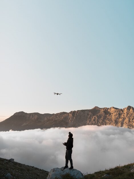 Un uomo con un drone in montagna che vola dietro le nuvole