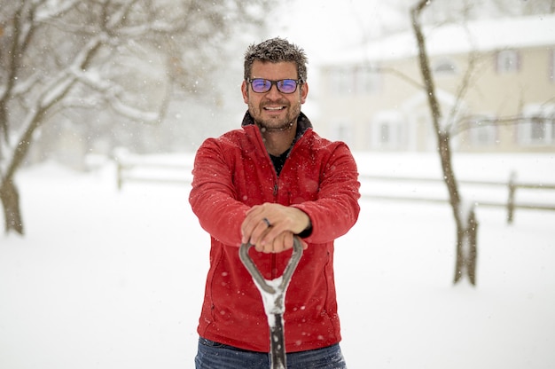 Un uomo con una giacca rossa sorridente e con in mano una pala da neve