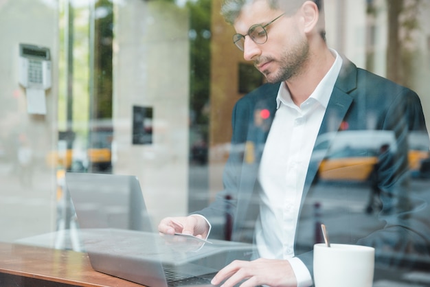 Un uomo d&#39;affari visto attraverso il vetro con carta di credito per lo shopping online nella caffetteria