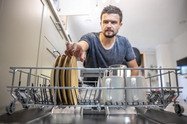 Un uomo davanti a una lavastoviglie aperta tira fuori o posa i piatti.