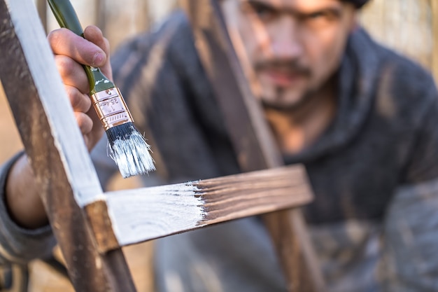 Un uomo dipinge con vernice bianca su assi di legno. Uomo nel concetto industriale. C'è un posto per il testo, l'oggetto è vicino