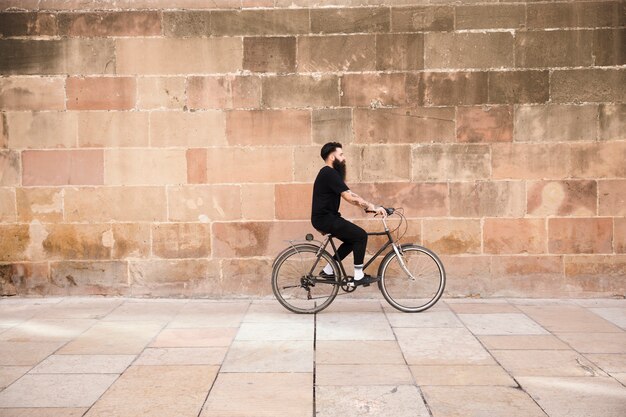 Un uomo in abiti neri in sella alla bicicletta di fronte al muro