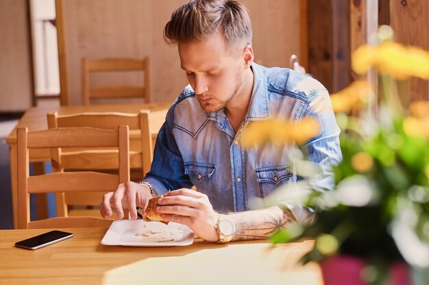 Un uomo in giacca di jeans mangia hamburger vegani.