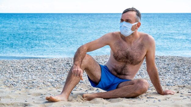 Un uomo in maschera medica bianca al mare