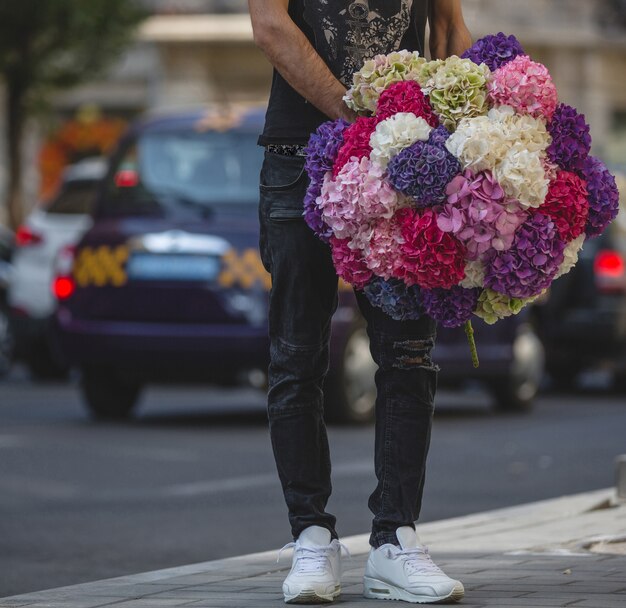 Un uomo in possesso di un grande mazzo di fiori di crisantemi colorati per la strada.