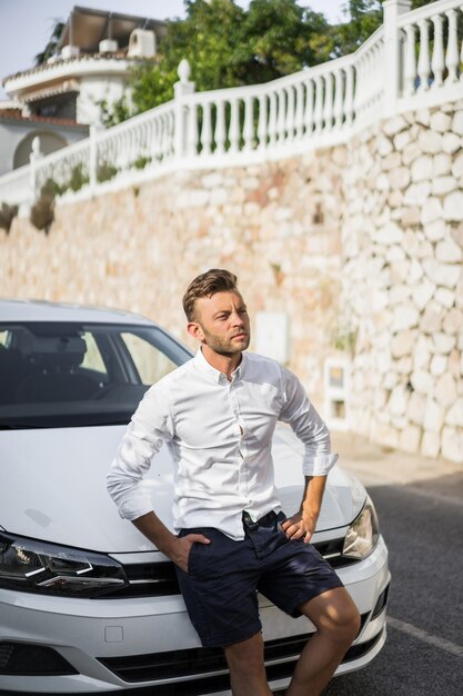 un uomo in una camicia bianca è seduto sul cofano di una macchina.