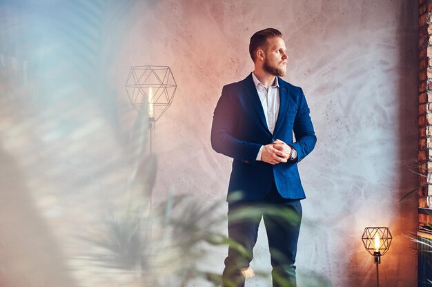 Un uomo moderno ed elegante vestito con un abito elegante in posa in una stanza con interni soppalcati.