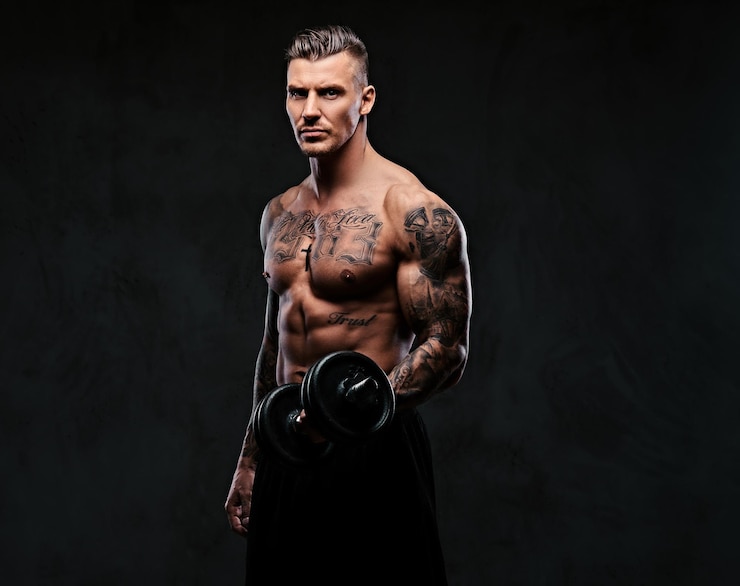 Foto gratuito un uomo muscoloso tatuato che fa esercizi con manubri per bicipiti su sfondo scuro.