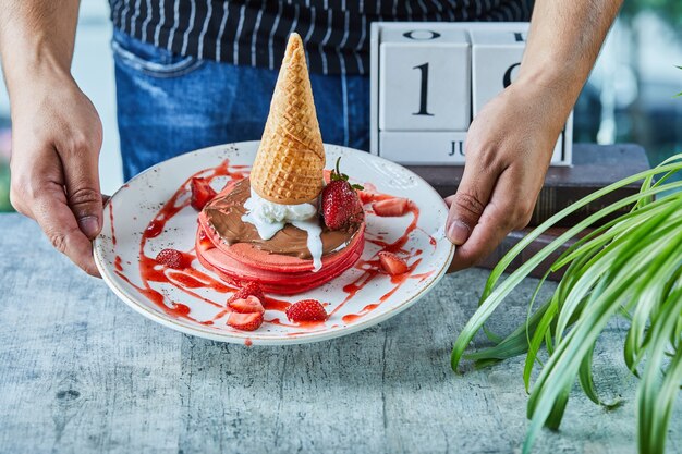 Un uomo passa in possesso di un piatto bianco con frittelle e fragole, cono gelato