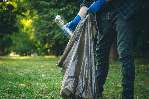 Un uomo ripulisce la foresta getta una bottiglia in un primo piano del sacco della spazzatura