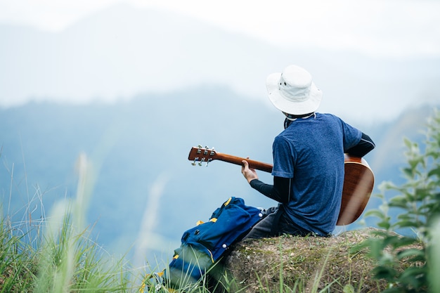 Un uomo seduto felicemente a suonare la chitarra nella foresta da solo.