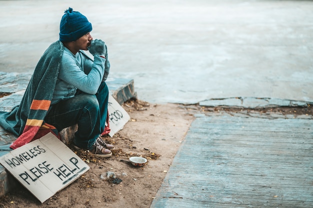 Un uomo seduto mendicanti con senzatetto per favore aiuto messaggio.