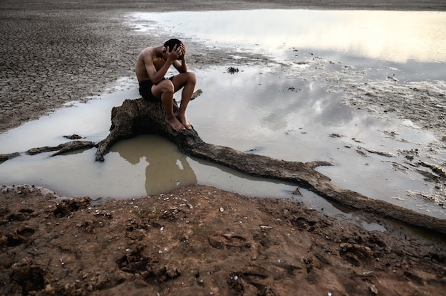 Un uomo seduto piegò le ginocchia e mise le mani sulla testa, sulla base dell'albero e circondato dall'acqua.