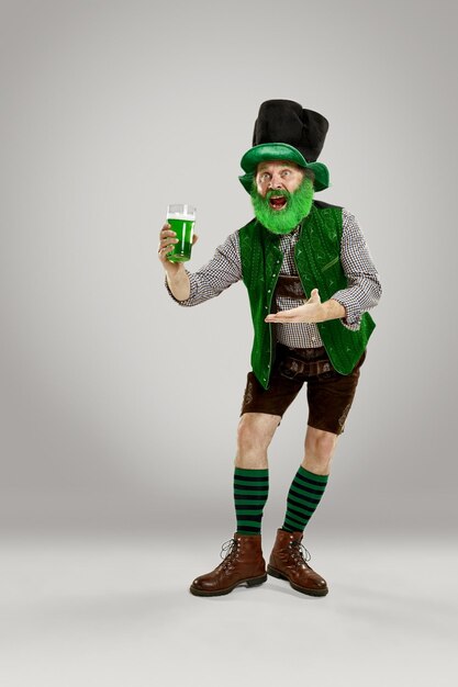 Un uomo senior felice sorridente in un cappello del leprechaun con birra verde allo studio. Celebra il giorno di San Patrizio. La celebrazione, la festa, la birra, le vacanze, l'alcol, il concetto di festa
