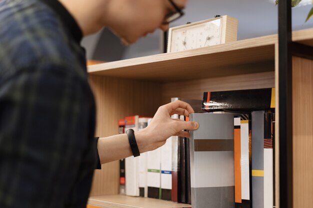 Un uomo studente raccogliendo libri dallo scaffale