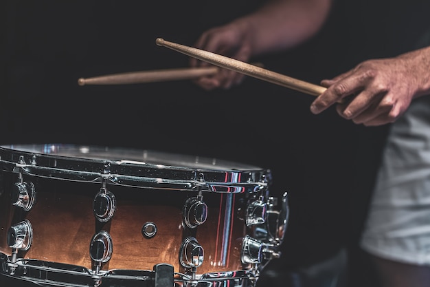 Un uomo suona un rullante con dei bastoncini, un batterista suona uno strumento a percussione, primo piano.