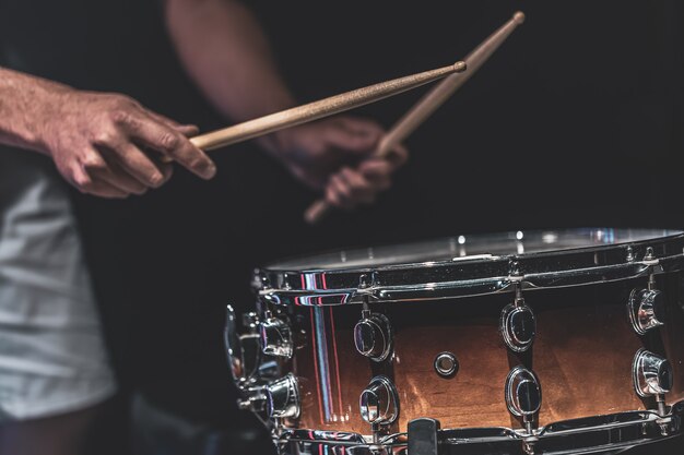 Un uomo suona un rullante con dei bastoncini, un batterista suona uno strumento a percussione, primo piano.