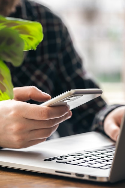 Un uomo tiene uno smartphone e lavora su un laptop