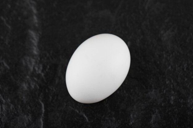 Un uovo di gallina bianco fresco su un tavolo nero.