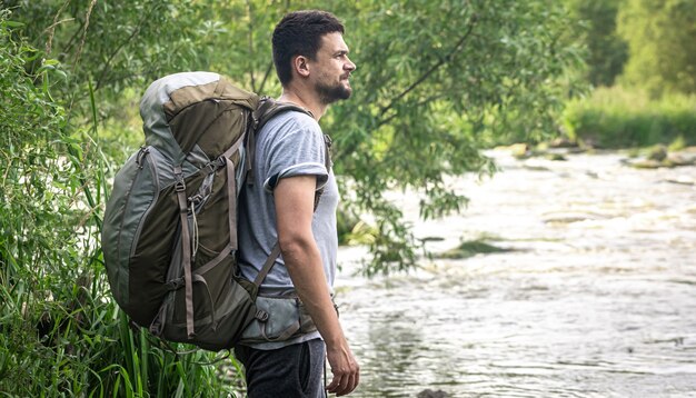 Un viaggiatore maschio con un grande zaino da trekking si trova vicino al fiume.