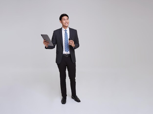 Un viso bello e amichevole, un uomo d'affari asiatico che sorride in abito formale, che usa un tablet e una tazza di caffè.