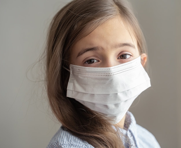 Una bambina carina con una maschera protettiva usa e getta dal coronavirus