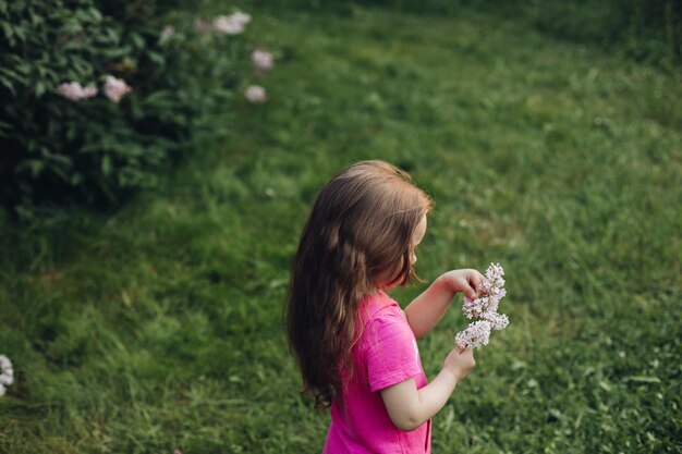 Una bambina carina in un vestito rosa in un parco verde in primavera o in estate