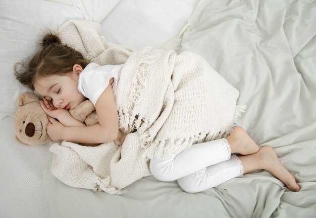 Una bambina carina sta dormendo in un letto con un orsacchiotto. Concetto di sviluppo del bambino e sonno. La vista dall'alto.