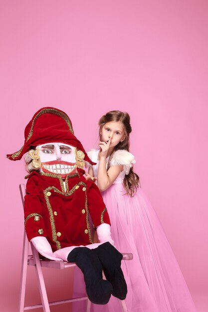 Una bambina come ballerina di bellezza in abito lungo rosa con schiaccianoci in studio rosa