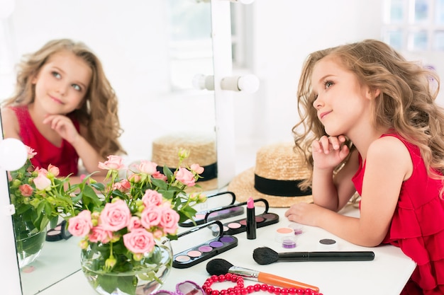 Una bambina con abito rosso e cosmetici.