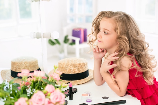 Una bambina con cosmetici seduti vicino allo specchio.