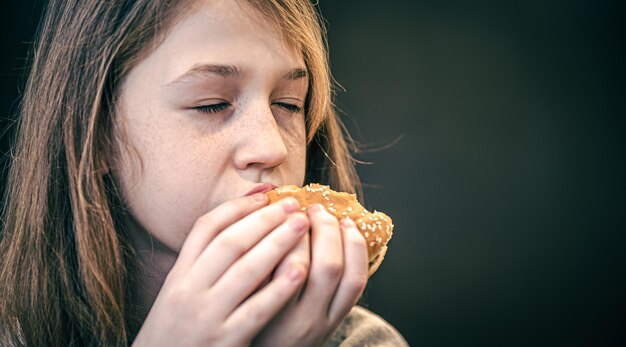 Una bambina con le lentiggini mangia un hamburger