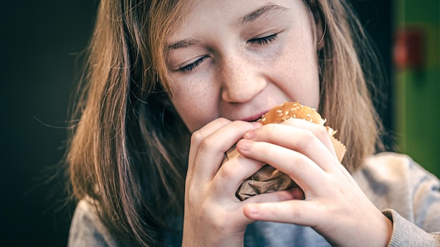 Una bambina con le lentiggini mangia un hamburger